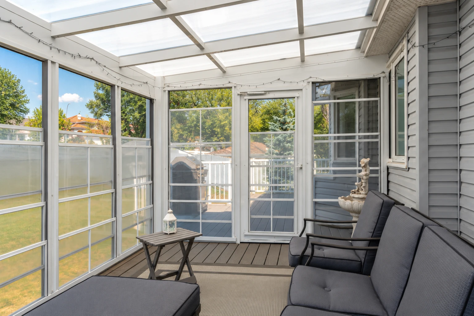 Enclosed patio room with a translucent roof, white-framed screened walls, gray seating and a wooden floor.