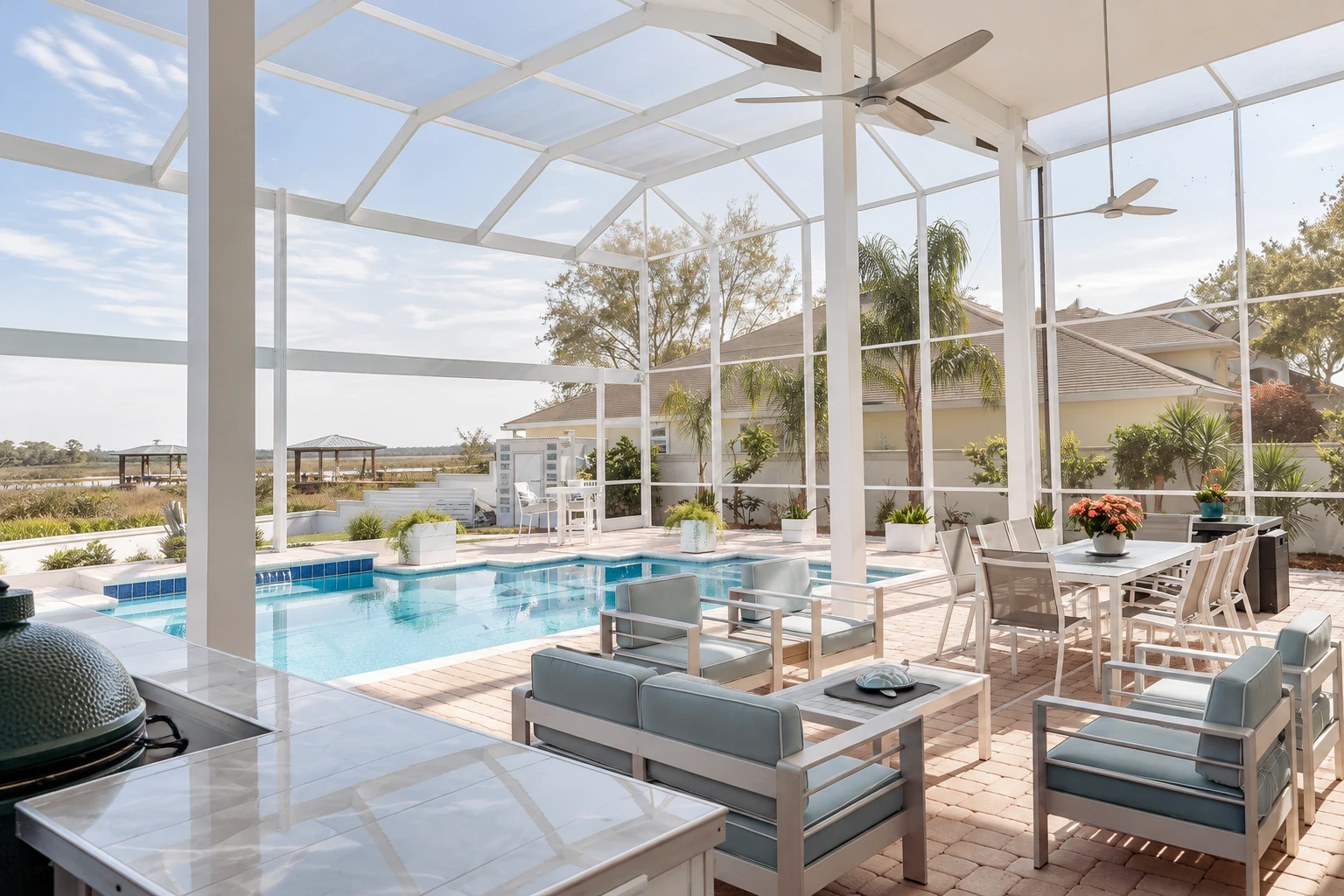A bright solarium with white framing encloses a pool and patio furnished with lounge chairs, dining table, and ceiling fans.
