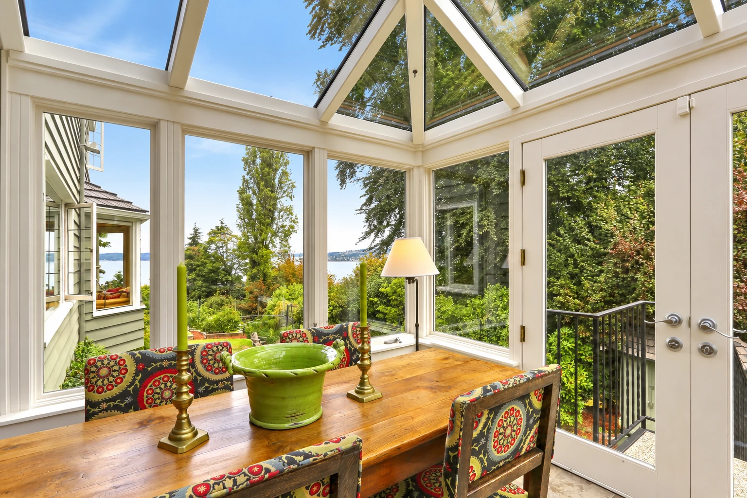 Bright sunroom with a peaked glass roof, a wooden dining table, patterned chairs and garden views through tall windows.