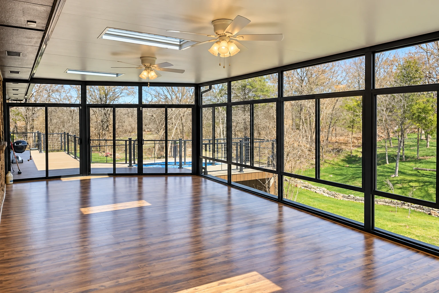 A remodeled sunroom features black-framed windows, polished wood flooring, ceiling fans and views of a yard and pool.